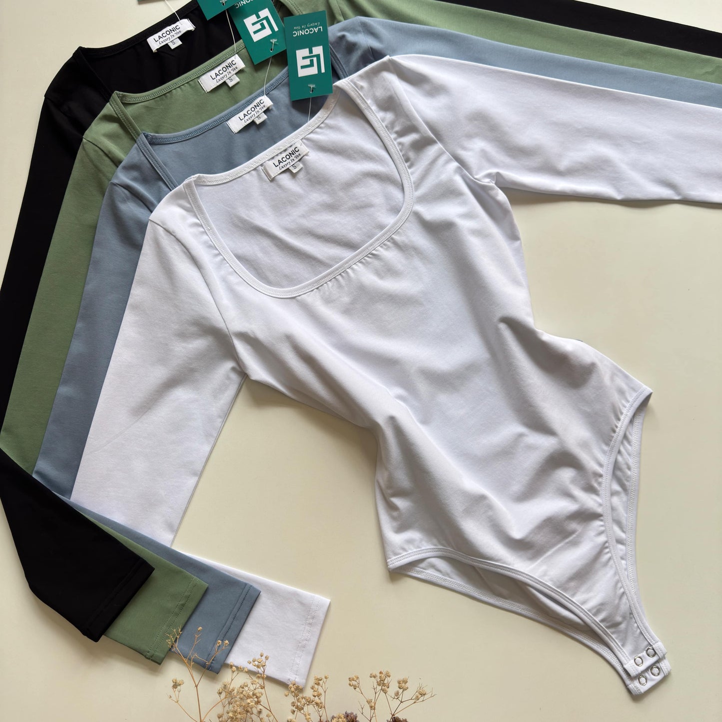 A collection of square neck full sleeve bodysuits by Laconic Fashion Nepal, cotton lycra fabric, best basic bodysuit in black, white, green, and gray, displayed on hangers against a neutral background. online shopping and in store visit